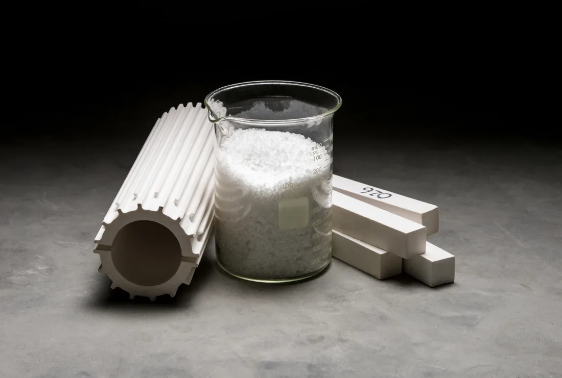 Fused silica tube and shapes next to a beaker of raw material
