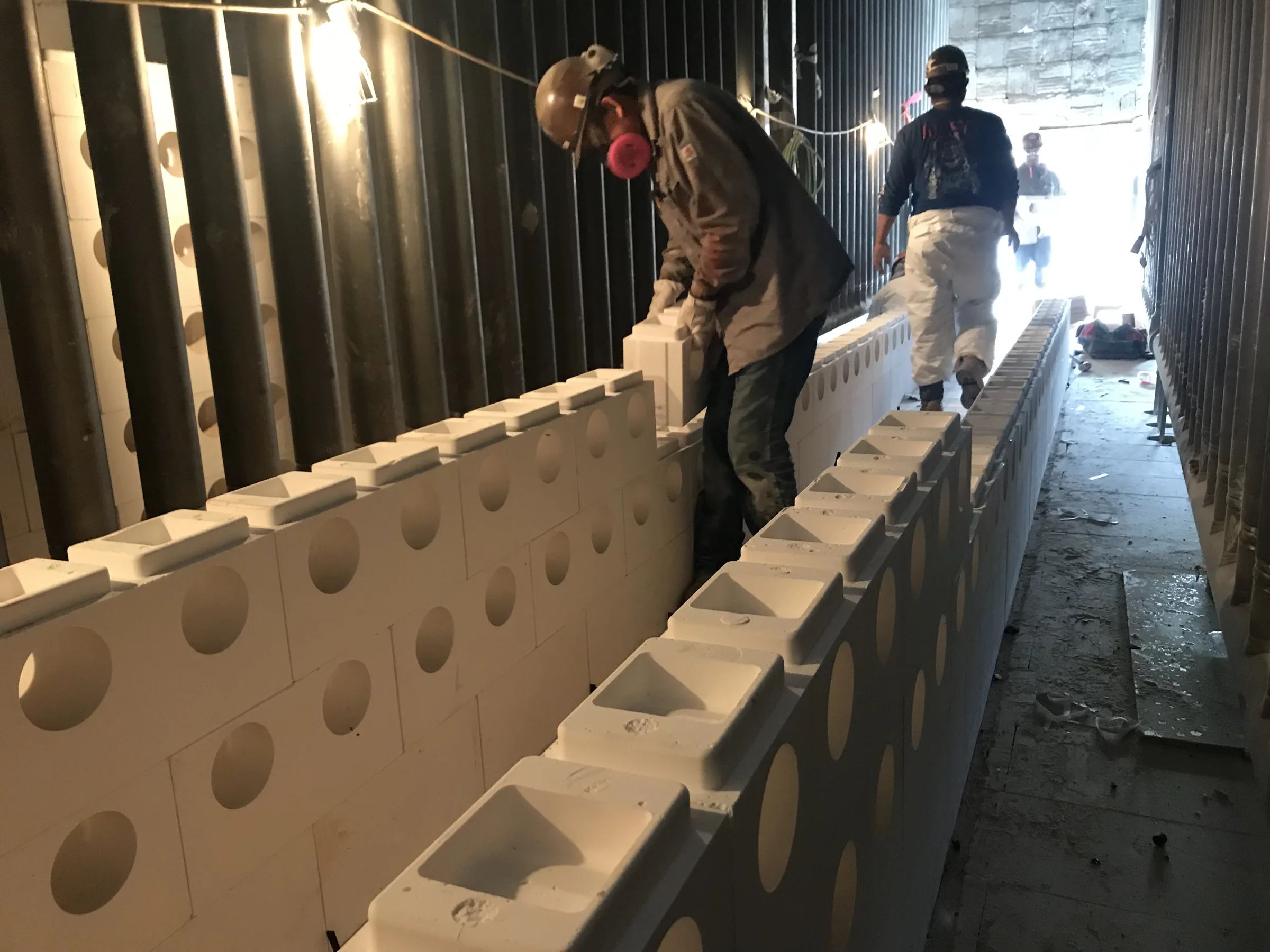 Two workers setting precast tunnel blocks inside a reformer furnace