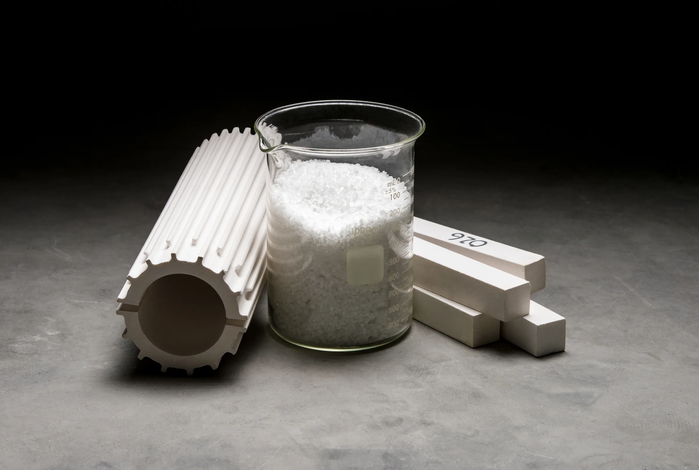 Fused silica tube and shapes next to a beaker of raw material